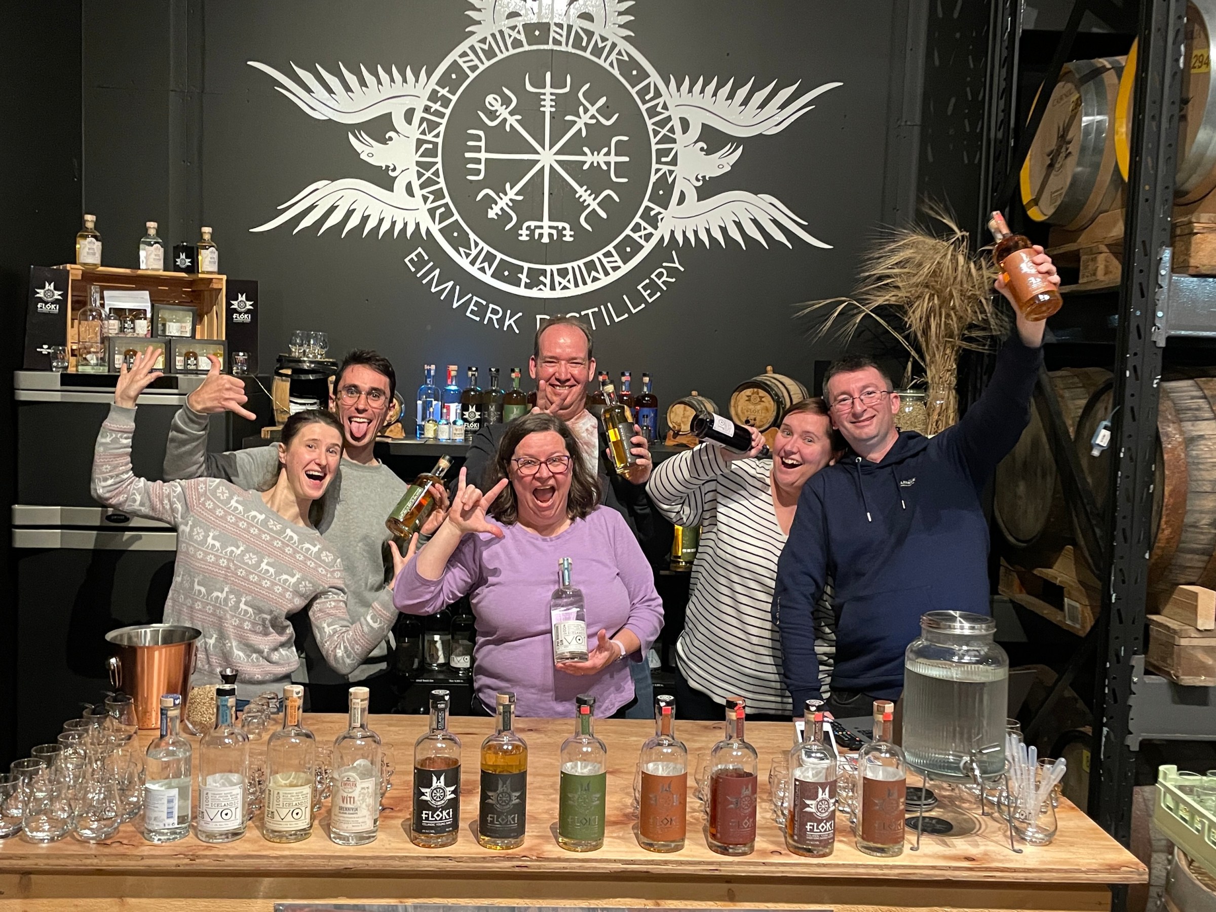 Group of people celebrating at a distillery with bottles and barrels.