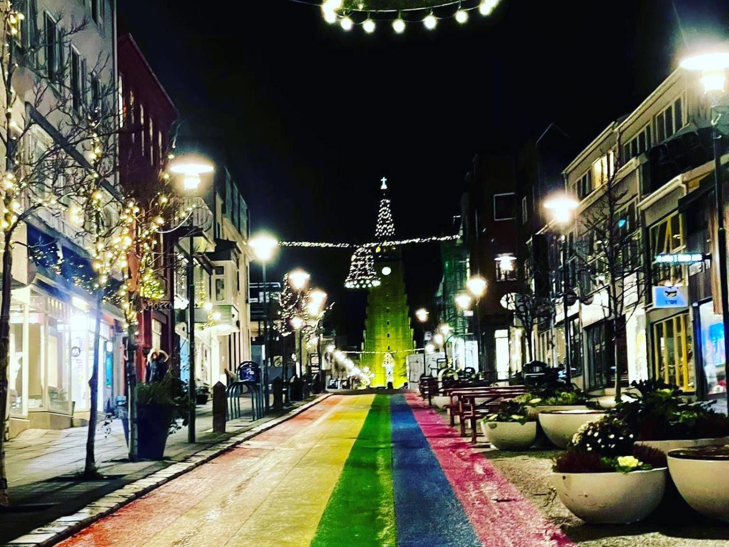 Night street scene with rainbow-colored road and festive lights.