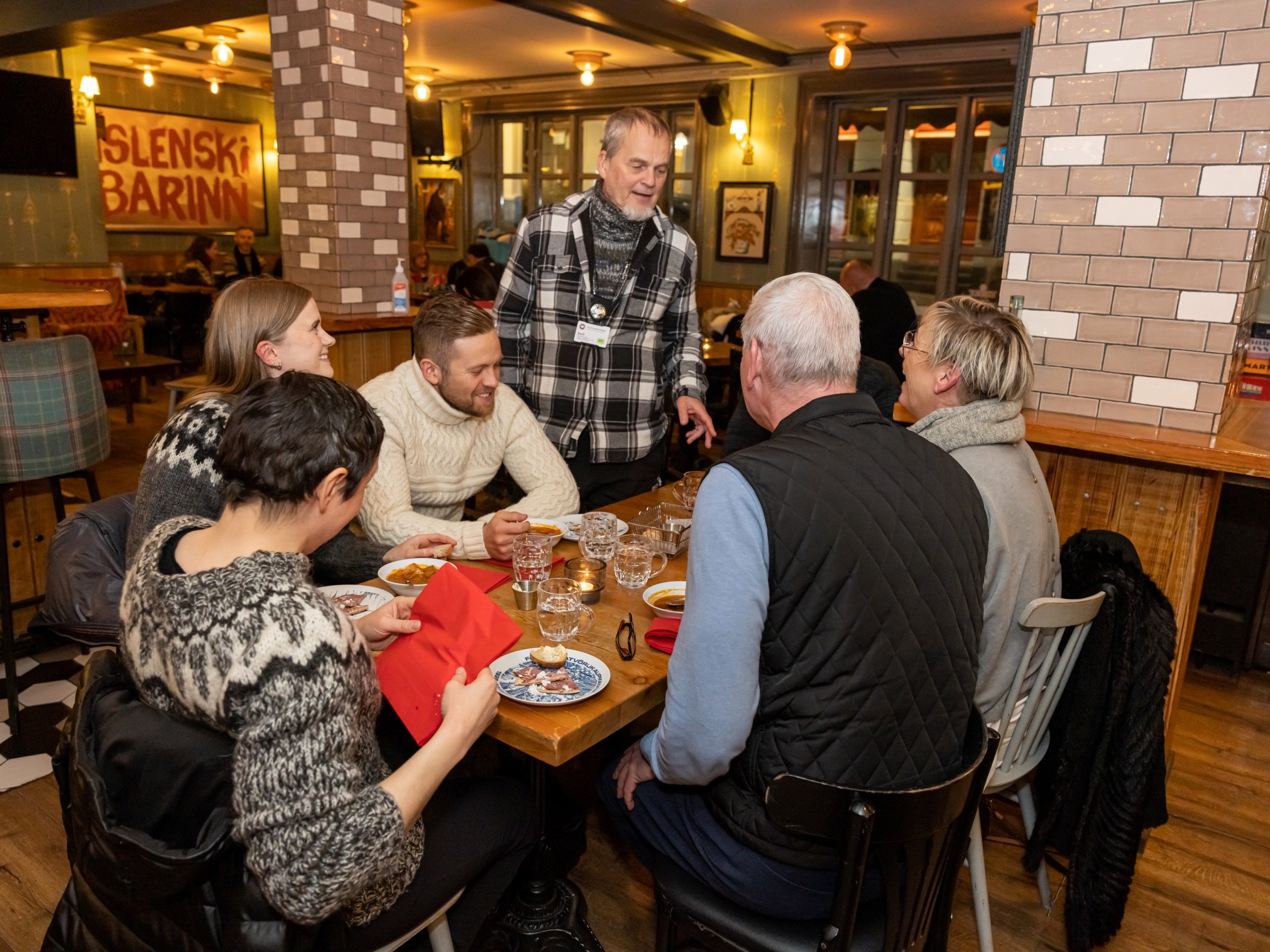 Group of people dining at a cozy restaurant, engaging in conversation around a wooden table.