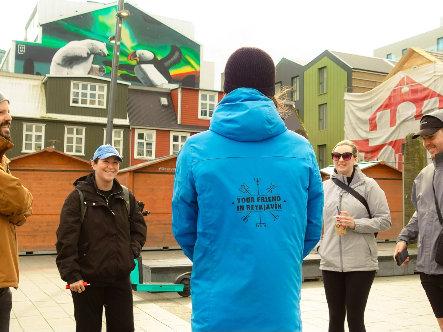 People in jackets stand together outside near colorful buildings in Reykjavik.