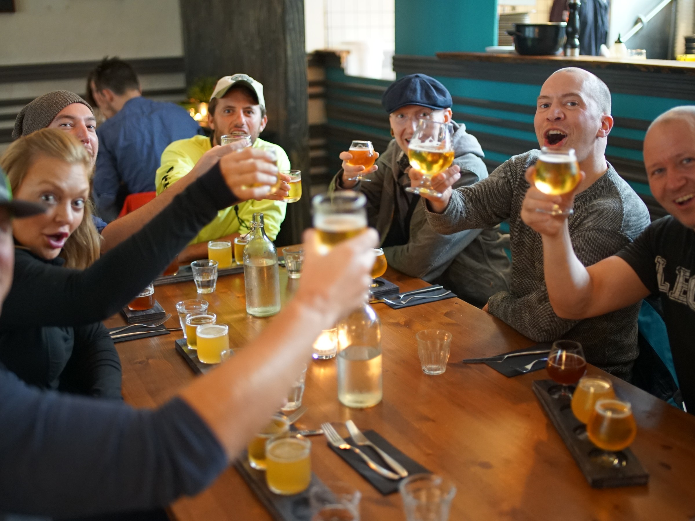 Group of people toasting with beers around a restaurant table.