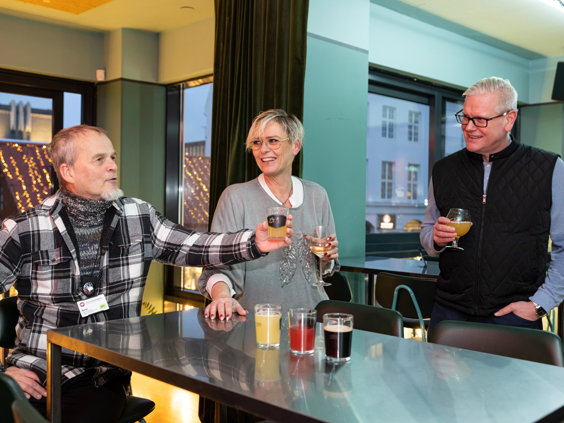 Three people at a bar table holding drinks, smiling and talking.