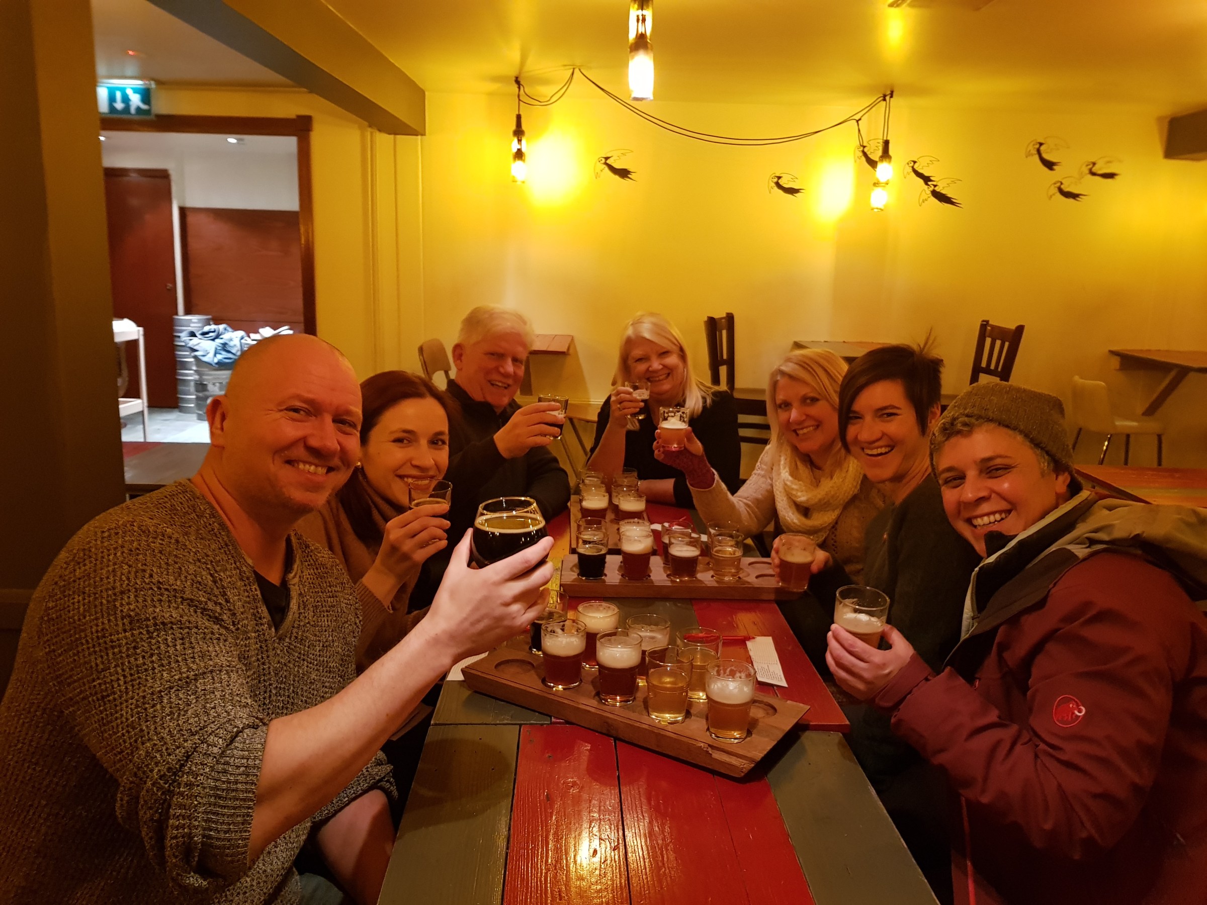 Group of people in a pub, smiling and holding glasses of beer.