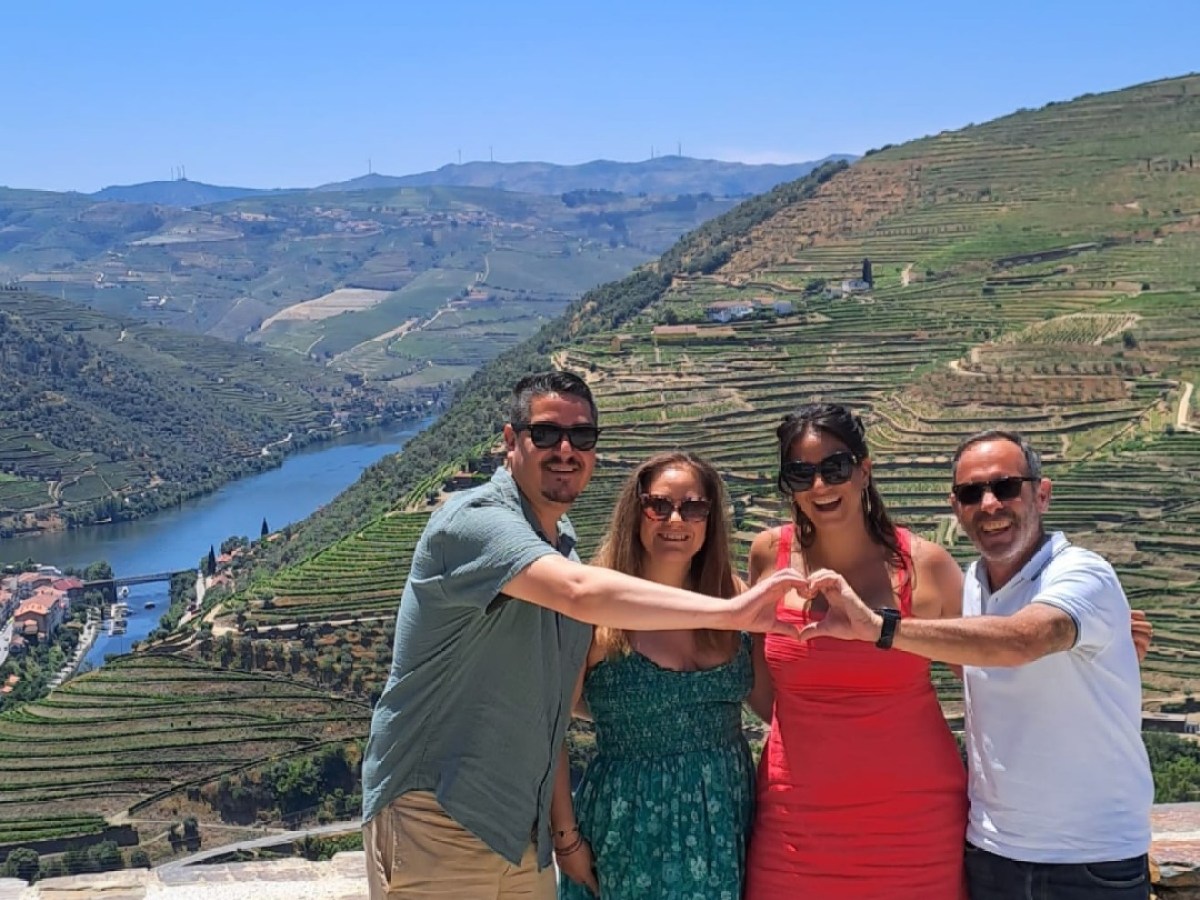 Four people making a heart shape with hands, overlooking terraced hills and river.
