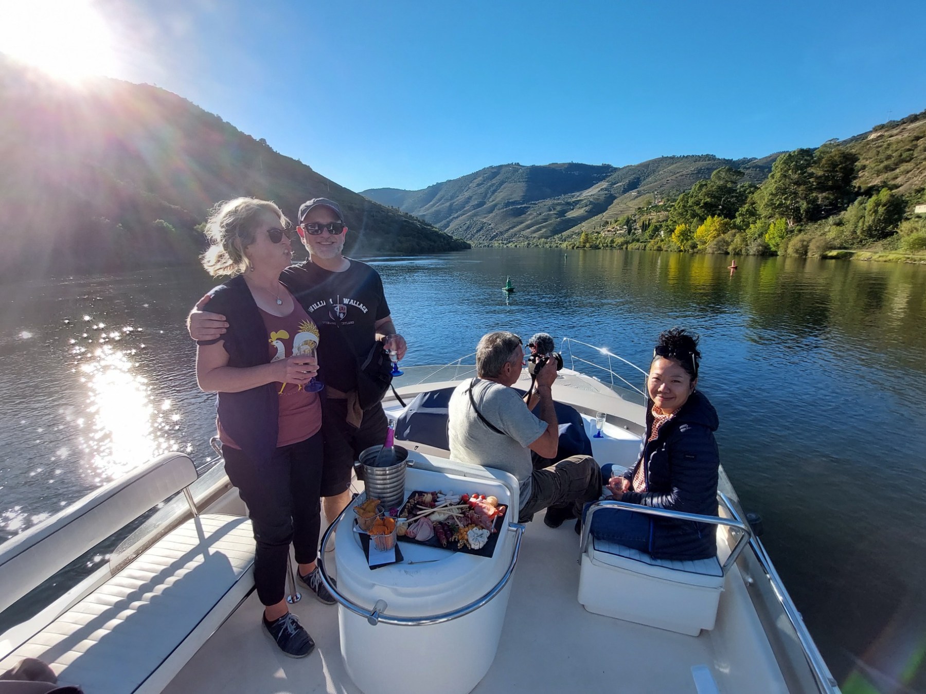 People on a boat enjoying a scenic river view with mountains under a clear blue sky.