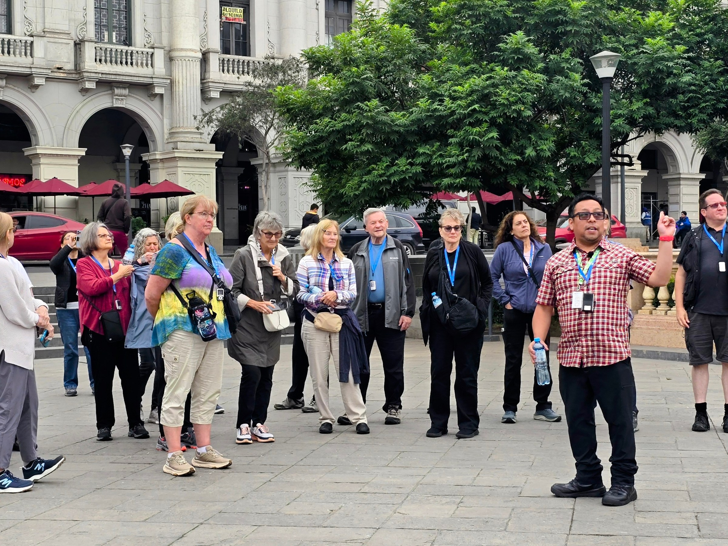 Tour group in a city square with a guide speaking, historic building in background.
