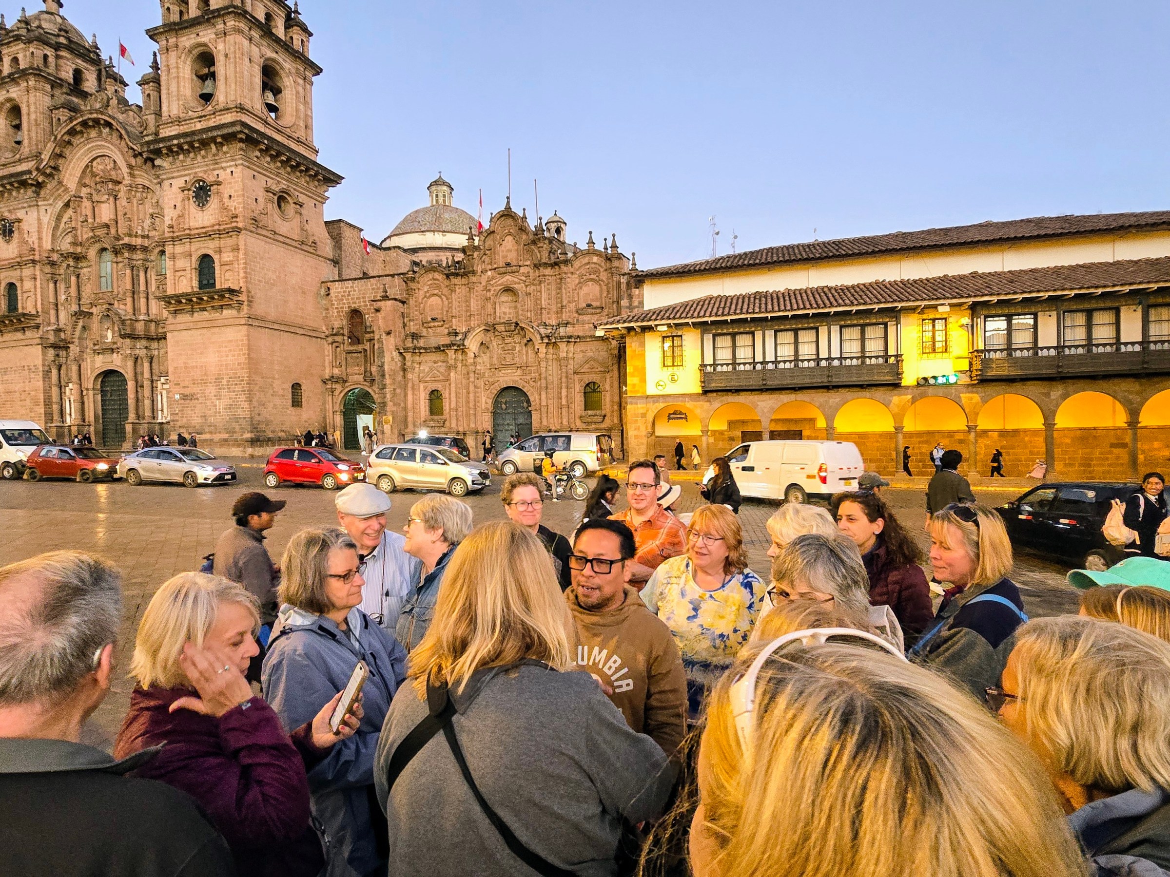 Tour group gathers in a plaza near historic buildings at dusk.