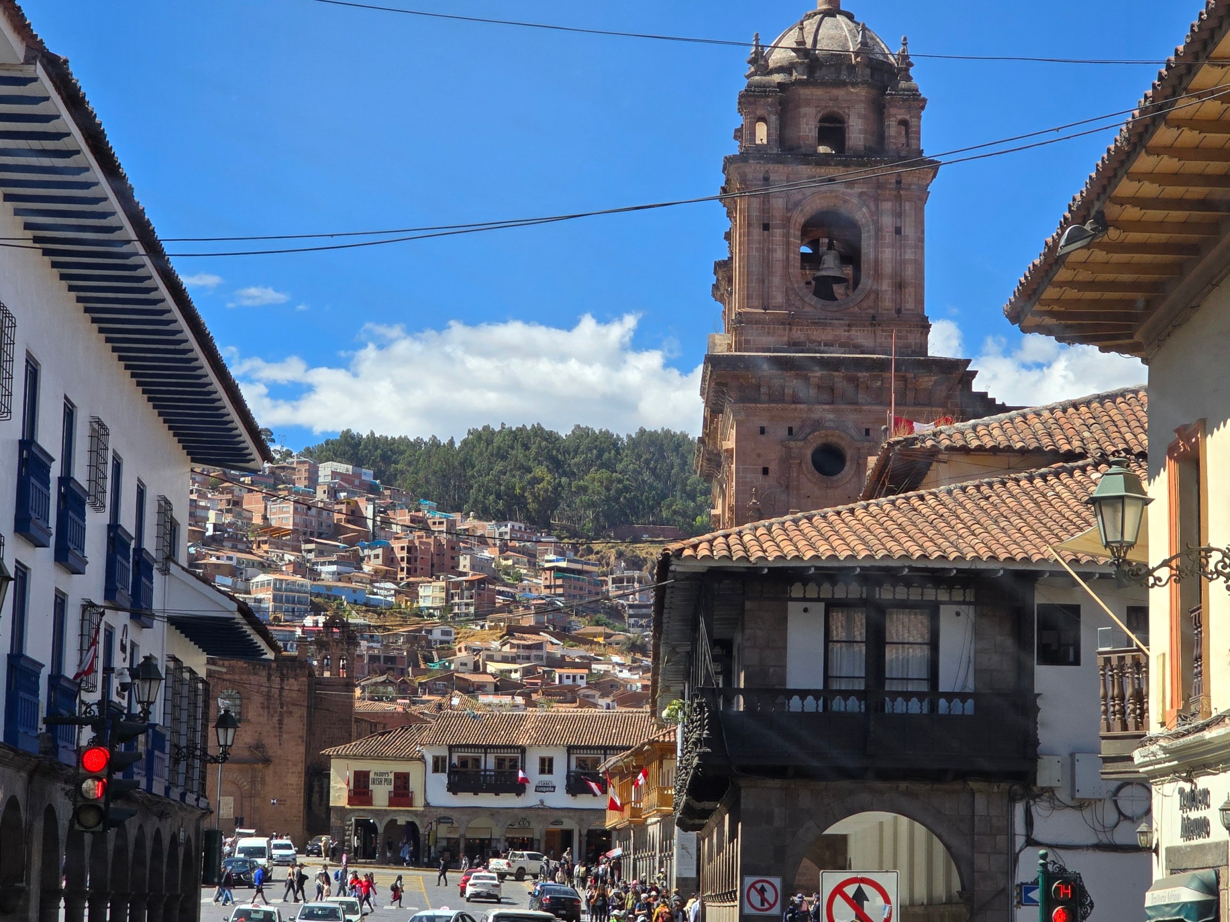 Street view of historic city with church tower and mountains in background.